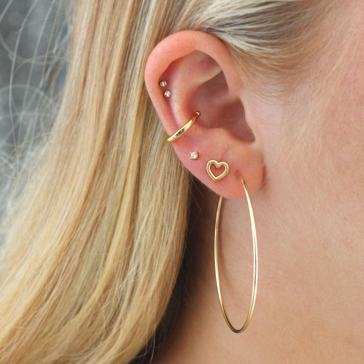 Model wearing a tiny gold heart stud, closer crop