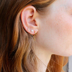 Model wearing small gold hoops with spike charms