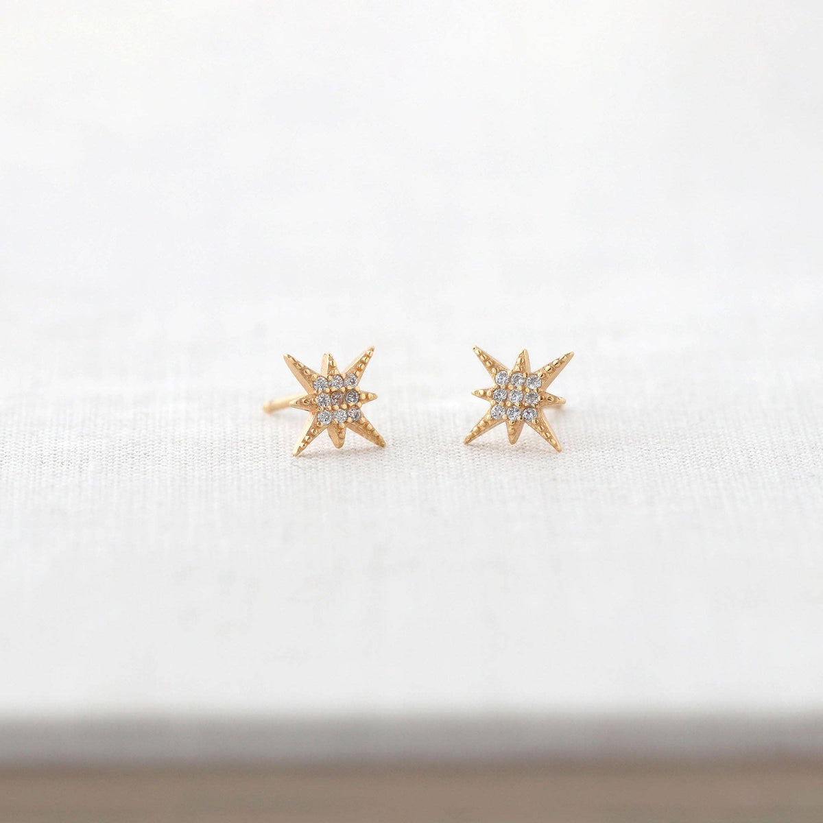 Starburst Crystal Stud Earrings in gold vermeil resting on a white book